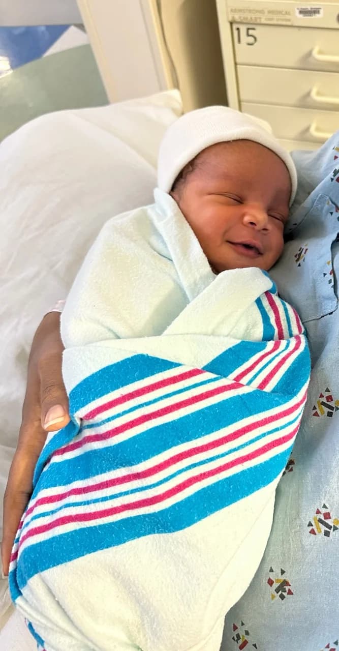 Newborn Mykah wearing a white cap and wrapped in a striped hospital blanket